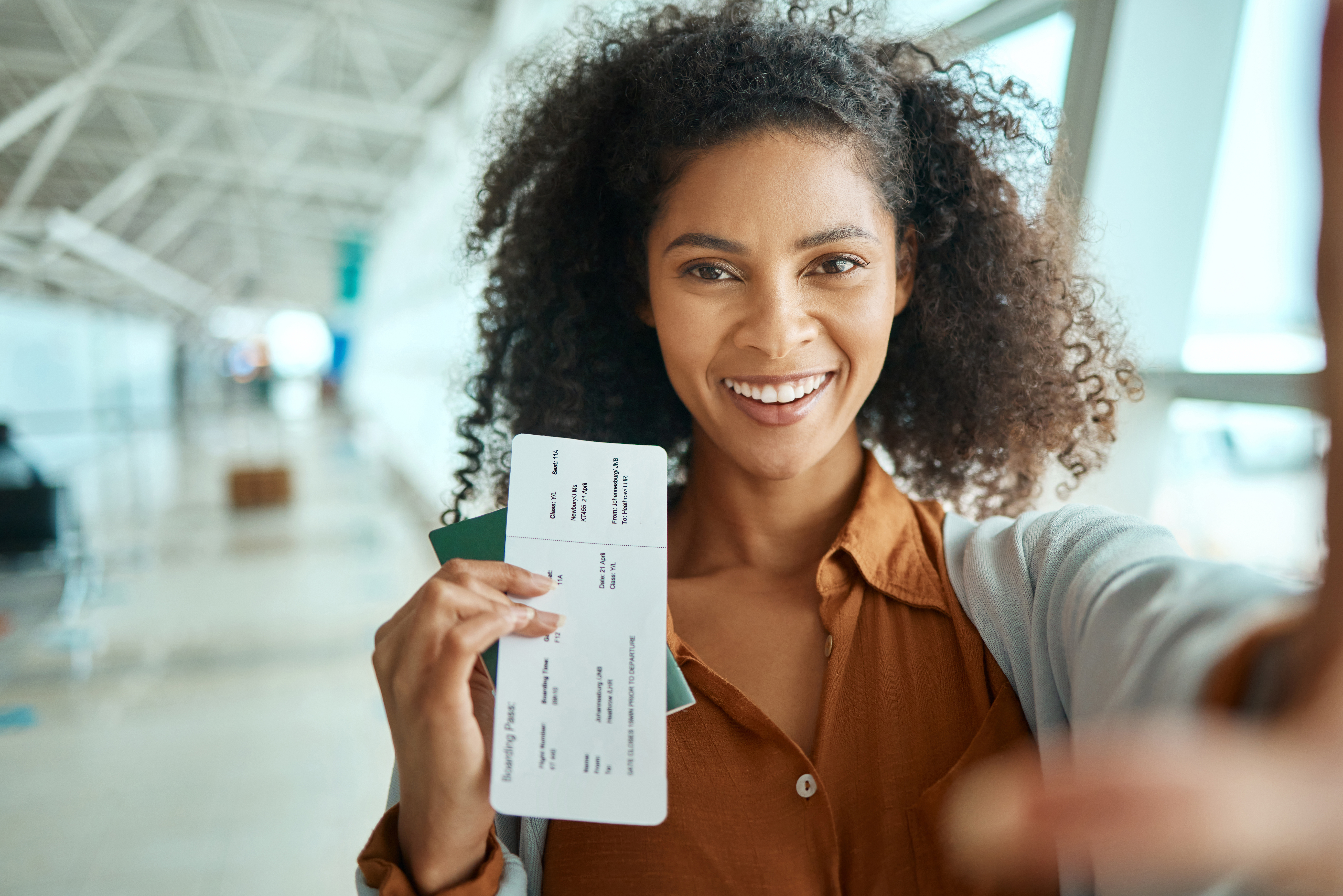 Een lachende vrouw houdt haar vliegticket vast in een luchthaven, klaar voor vertrek.
