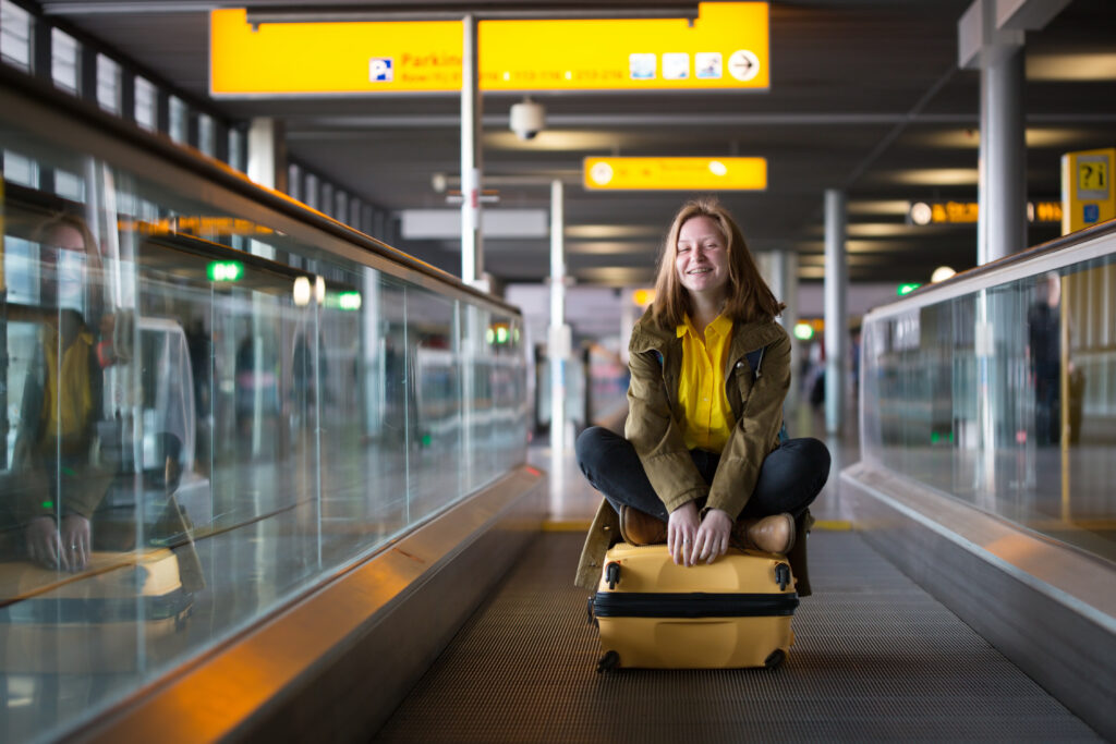 Vrouw met gele koffer op Schiphol, klaar om te reizen naar populaire bestemmingen vanuit Amsterdam.