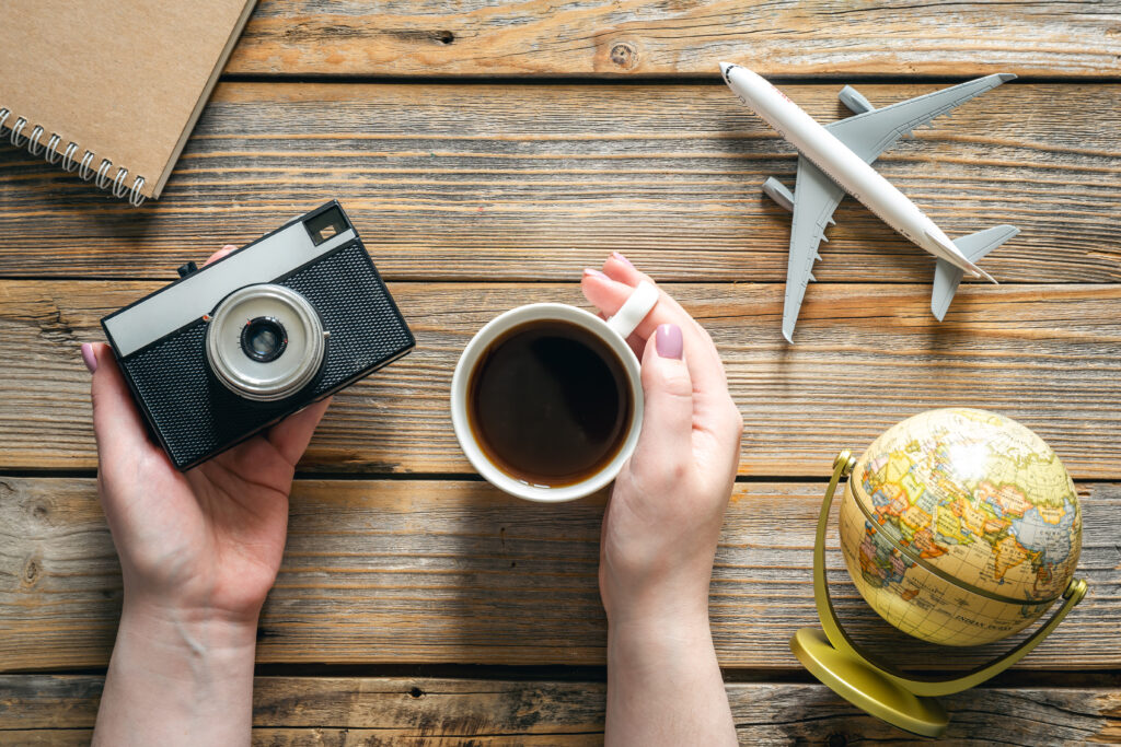Reisbenodigdheden: vintage camera, een kop koffie, een wereldbol en een vliegtuigmodel op een houten tafel.