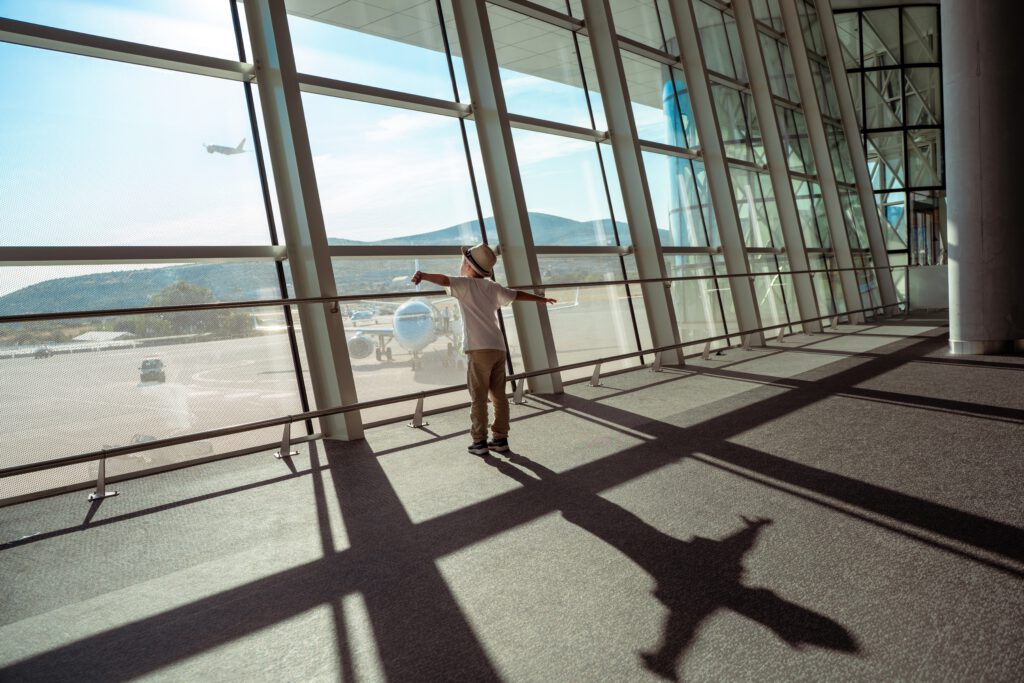 Kind kijkt uit over de luchthaven terwijl een vliegtuig opstijgt, perfect voor het boeken van voordelige last-minute vluchten via Vlucht-Ticket.nl.