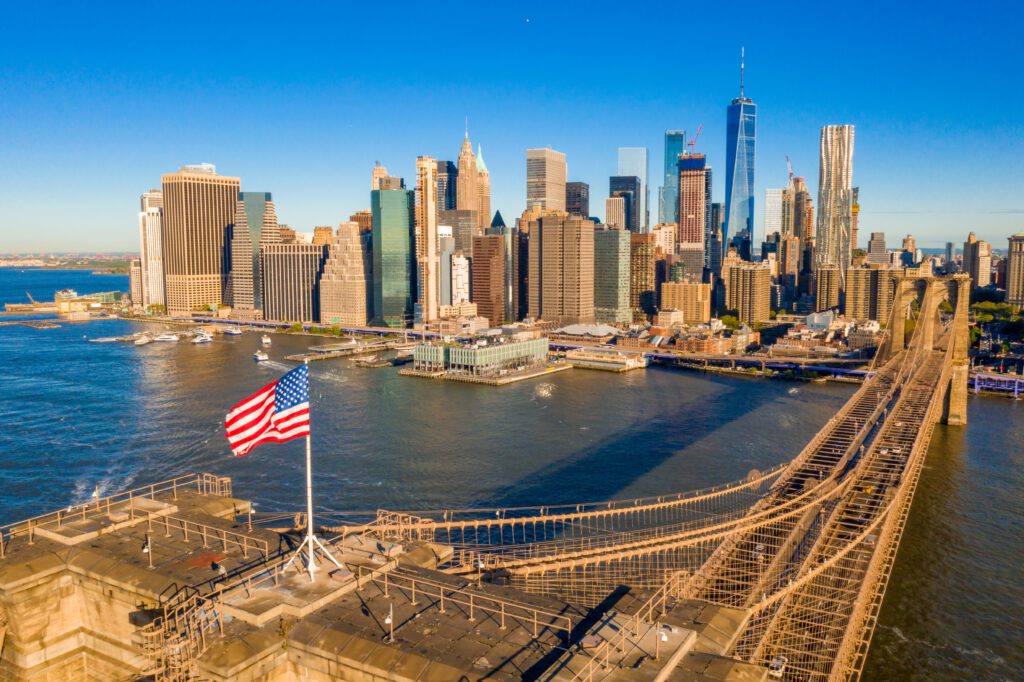 Uitzicht op de Brooklyn Bridge en de skyline van Manhattan in New York City, met de Amerikaanse vlag op de voorgrond.