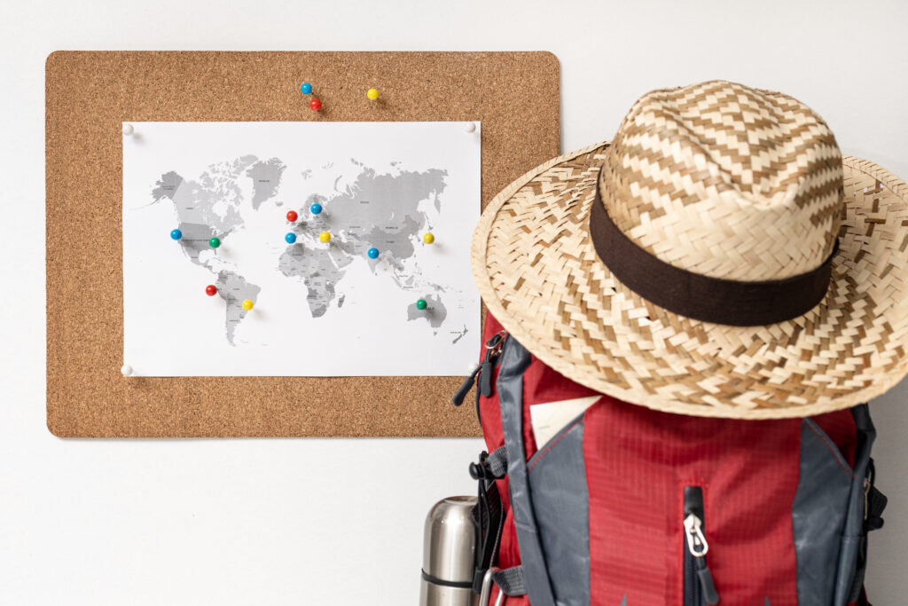 Wereldkaart met speldjes en een backpack, symbool voor het plannen van reizen naar betaalbare hotels wereldwijd.