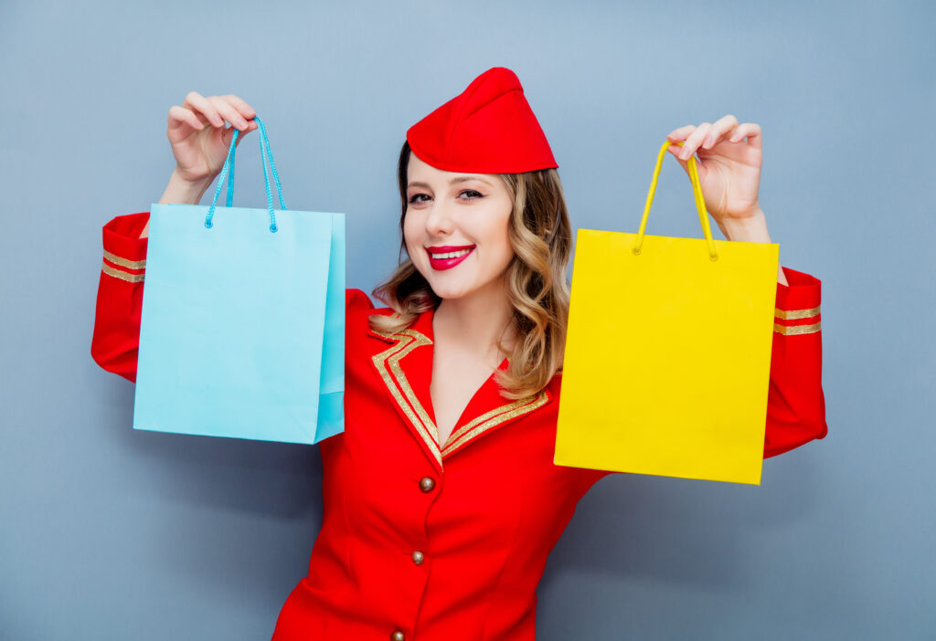Stewardess in een rode uniform met blauwe en gele shoppingtassen, symbool voor beloningen uit loyaliteitsprogramma's.