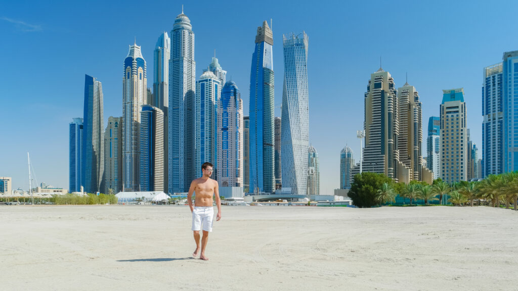 Man wandelt over het strand in Dubai, met de moderne skyline op de achtergrond, ideaal voor een luxe last minute reis.