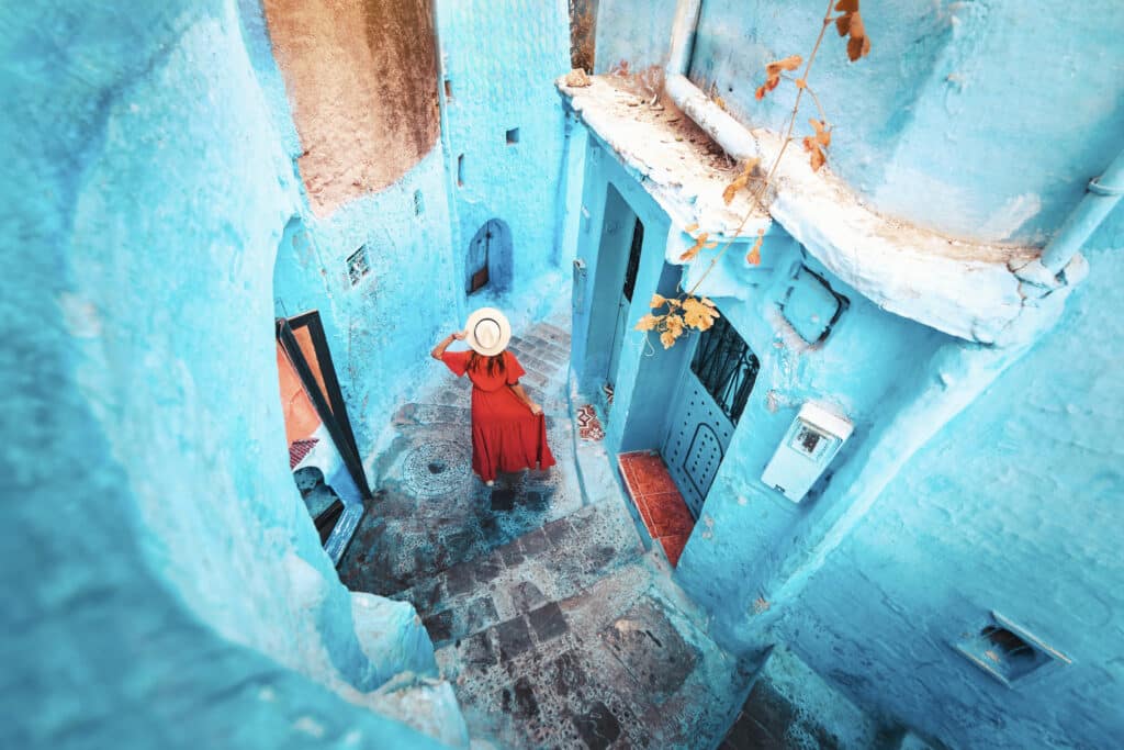 Vrouw in rode jurk verkent de blauwe straatjes van Chefchaouen – vliegtickets bestemming Marokko