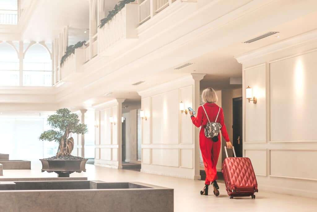 Vrouw in rood pak arriveert met koffer in luxe hotel – top 10 beste luxe hotels in Spanje