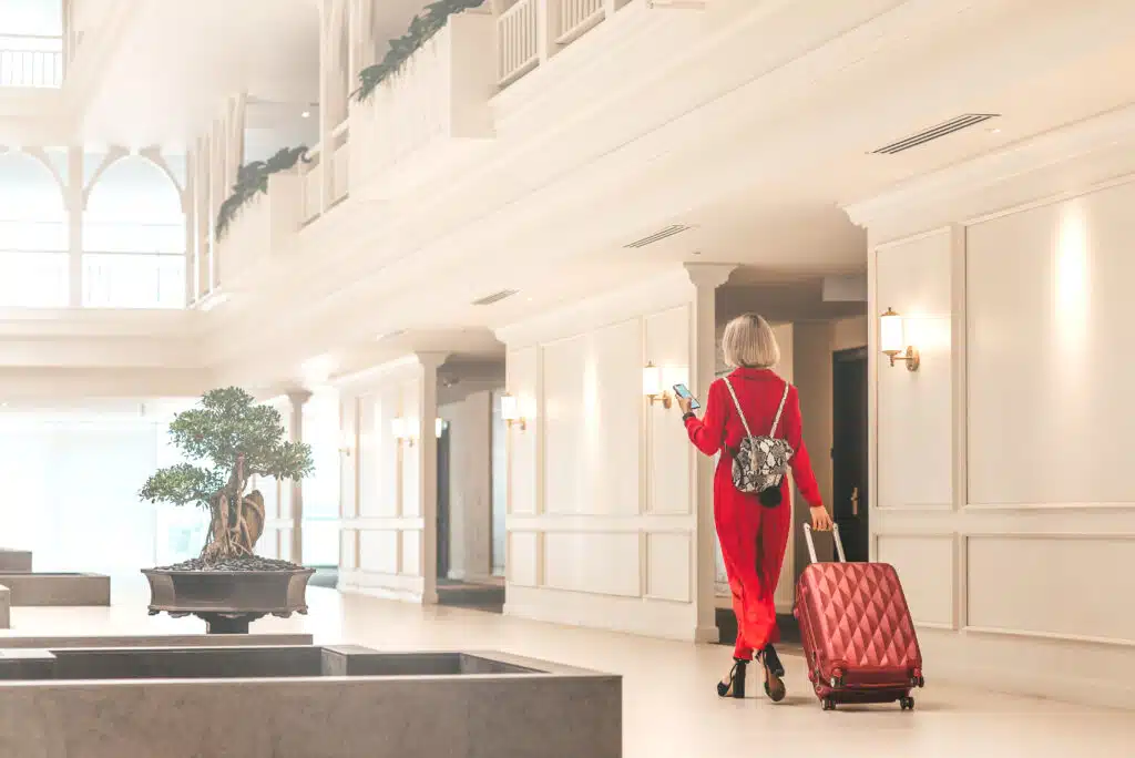 Vrouw in rood pak arriveert met koffer in luxe hotel – top 10 beste luxe hotels in Spanje