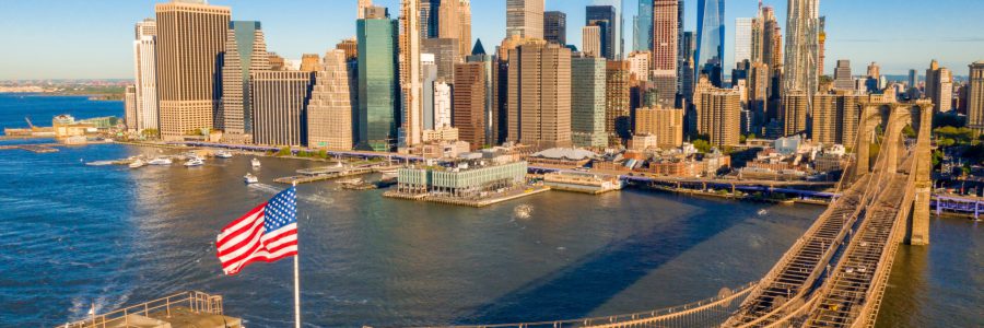Uitzicht op de Brooklyn Bridge en de skyline van Manhattan in New York City, met de Amerikaanse vlag op de voorgrond.