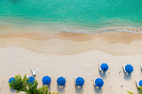 Caribisch strand met blauwe parasols en turquoise water, perfect voor een luxe vakantie via Vlucht-Ticket.nl.